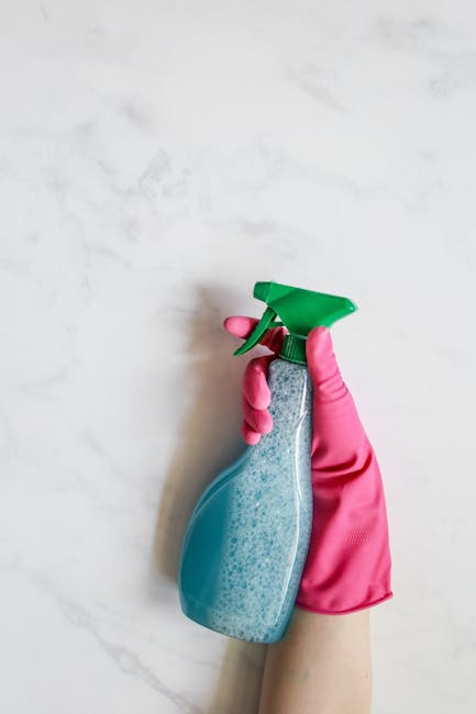 A light blue dustpan and a wooden-handled brush with natural bristles are hanging on a white wall, likely in a domestic or commercial cleaning setting. The dustpan is positioned with its opening facin
